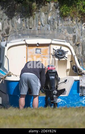 Un propriétaire de bateau travaillant sur son petit bateau à moteur amarré sur la rivière Gannel à marée basse à Newquay en Cornouailles. Banque D'Images