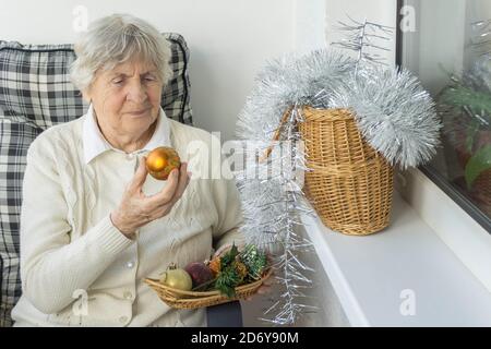 Cheveux gris femme sénior assis dans une chaise et tenant le jouet de Noël. La vieille femme se prépare pour Noël et le nouvel an. Banque D'Images