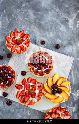 Tartelettes fraîches et délicieuses de cerises, fraises et pêches sur fond gris Banque D'Images
