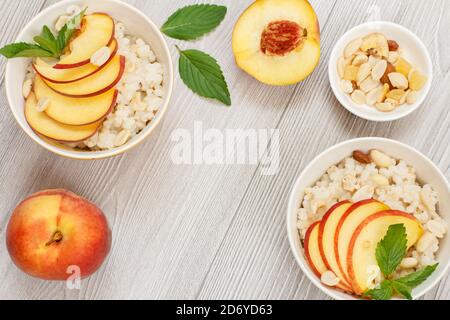 Porridge de sorgho avec morceaux de pêche, noix de cajou et amandes dans des bols en porcelaine, pêches fraîches sur des planches en bois. Salade végétalienne de sorgho sans gluten avec Banque D'Images