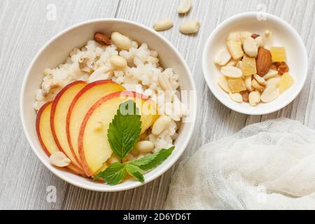 Porridge de sorgho avec des morceaux de pêche, noix de cajou et amande dans des bols en porcelaine sur des planches de bois gris. Salade de sorgho végétalienne sans gluten avec fruits. Banque D'Images