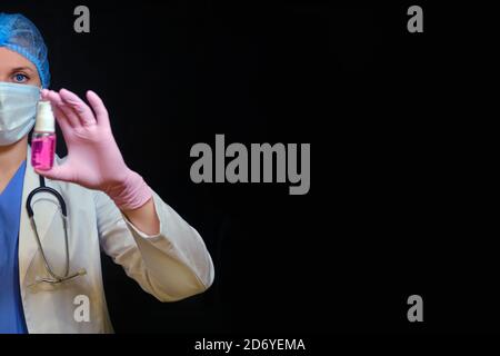 Une infirmière vaporise une bombe de désinfectant rouge, fond noir. Médecin en gants médicaux avec désinfectant, gros plan. Concept d'hygiène des mains pour coronavirus pa Banque D'Images