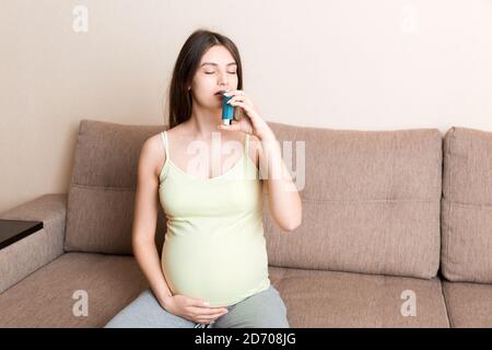 femme enceinte utilisant un inhalateur d'asthme pendant l'attaque pour être en bonne santé sur le canapé à la maison. Concept de soins de santé du millénaire en santé. Banque D'Images