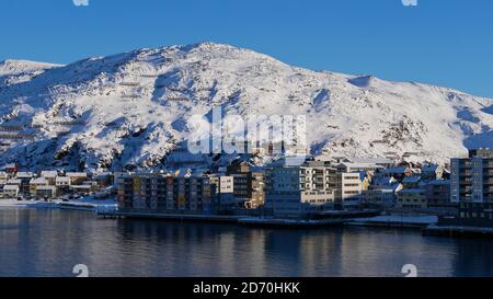 Vue de face des bâtiments résidentiels situés sur la rive à Hammerfest, Norvège, Scandinavie sur la mer arctique avec des montagnes enneigées en hiver. Banque D'Images