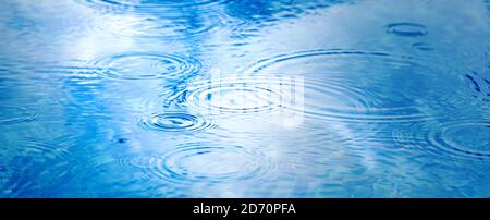 Gouttes de pluie sur la surface de l'eau bleu de la piscine. Texture de l'eau bleue comme arrière-plan. Taches les cercles sur l'eau de la pluie. Bande de toile longue Banque D'Images