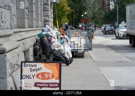 Un sans-abri assis sur le trottoir devant un immeuble. Banque D'Images