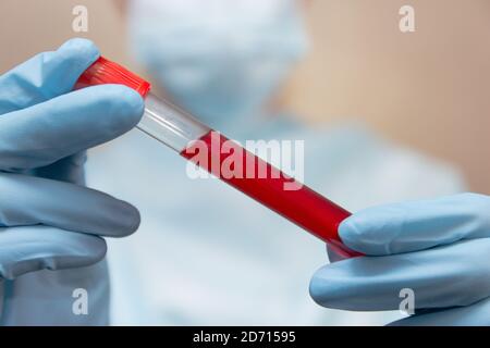 Test sanguin du coronavirus. Le médecin en costume de protection, masque médical et gants en latex tient un tube à essai avec du sang. Banque D'Images