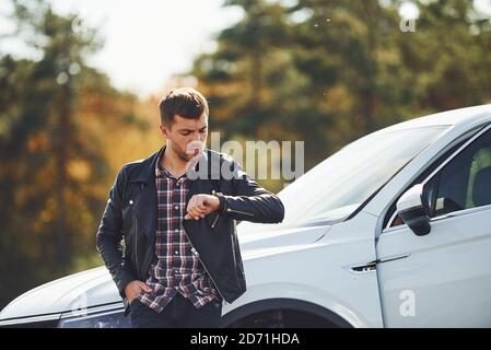 Homme en cuir noir se tient près de son parqué blanc voiture à l'extérieur et attend de l'aide Banque D'Images