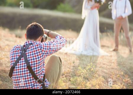 photographe professionnel prend des photos de la mariée et du marié dans la nature au coucher du soleil, photographe de mariage en action Banque D'Images