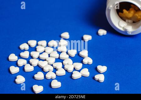 Des pilules en forme de coeur ont été déversées de la bouteille sur la surface bleue de la table à la pharmacie. Arrière-plan isolé. Arrière-plan bleu Banque D'Images