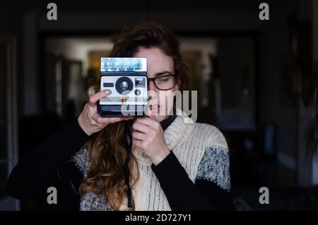 Fille caucasienne aux cheveux blonds foncés avec un vieux appareil photo polaroid à impression automatique. Banque D'Images