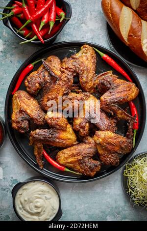 Ailes de poulet grillées au piment sur une assiette rustique servi avec diverses sauces et du pain Banque D'Images