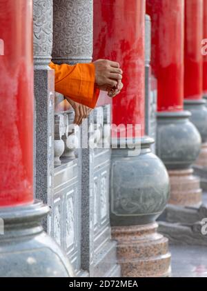 Rangée de colonnes dans un temple bouddhiste avec les mains d'un moine reposant sur une rampe, Thaïlande. Banque D'Images