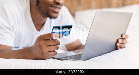 Black Man Shopping en ligne avec ordinateur portable et carte de crédit Indoor Banque D'Images