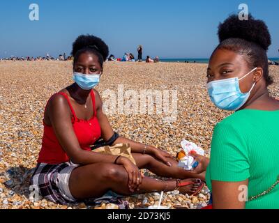 Des amis portant un visage couvrant s'assoient sur la plage de Hastings pour manger un McDonalds. Banque D'Images