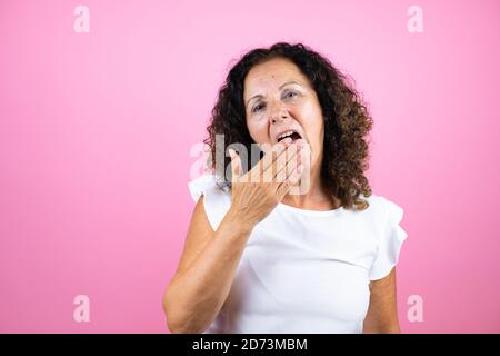 Femme d'âge moyen portant une chemise blanche décontractée debout sur un fond rose isolé ennuyé bâilling fatigué couvrant la bouche avec la main. Agité et somnine Banque D'Images