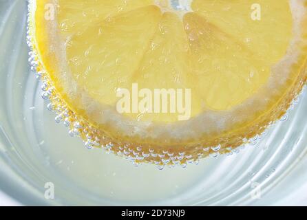 Détail de la tranche de citron avec bulles flottant sur l'eau dans un verre. Vue de dessus. Composition horizontale. Banque D'Images