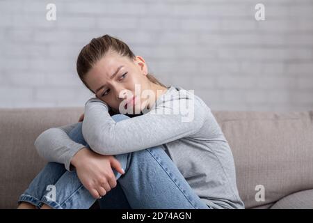 Dépression et anxiété concept. Jeune femme triste assise sur un canapé et embrassant ses genoux, espace de copie Banque D'Images