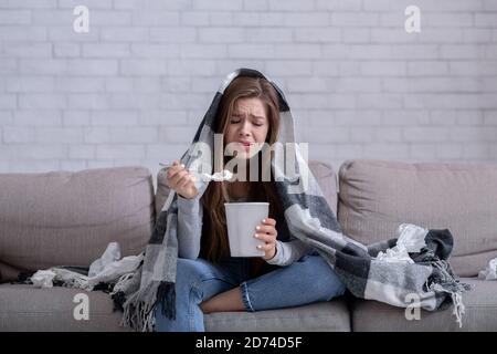 Concept de stress mangeant. Énervé femme mangeant de la crème glacée et pleurant sous le écossais chaud à la maison Banque D'Images