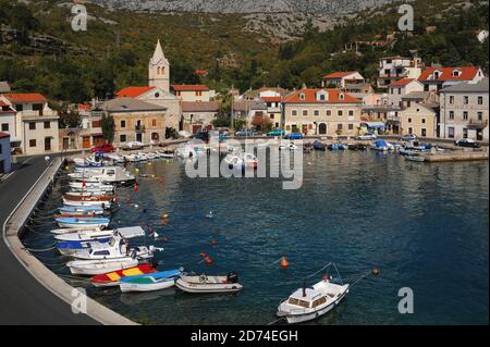 L'eau bleu-vert claire bordée de petits bateaux amarrés remplit le petit port de la côte Adriatique pittoresque de Jablanac, dans le comté de Lika-Senj, dans l'ouest de la Croatie. Le village, mentionné pour la première fois au XIIe siècle, se trouve sous la majeure partie de la chaîne de montagnes Velebit de 1,757 m (5,764 pi). Jusqu'en 1212, un ferry pour voitures et passagers reliait Jablanac à l'île offshore de Rab. Banque D'Images