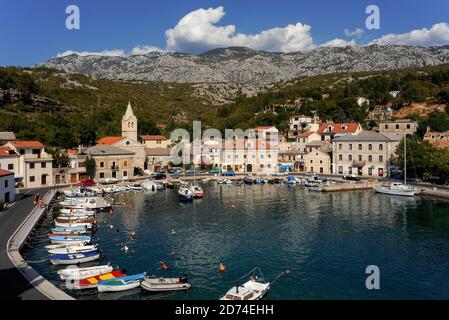 L'eau bleu-vert claire bordée de petits bateaux amarrés remplit le petit port de la côte Adriatique pittoresque de Jablanac, dans le comté de Lika-Senj, dans l'ouest de la Croatie. Le village, mentionné pour la première fois au XIIe siècle, se trouve sous la majeure partie de la chaîne de montagnes Velebit de 1,757 m (5,764 pi). Jusqu'en 1212, un ferry pour voitures et passagers reliait Jablanac à l'île offshore de Rab. Banque D'Images