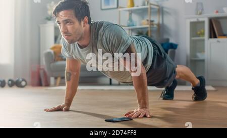 Athletic Fit Man en T-shirt et short fait des exercices push-up tout en utilisant un chronomètre sur son téléphone. Il est formation à la maison dans son salon avec