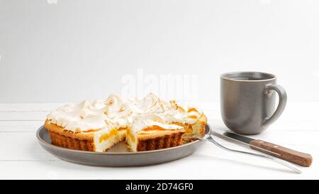 Tarte à l'abricot maison décorée de meringue et d'une tasse de thé sur une table en bois blanc. CopySpace. Banque D'Images