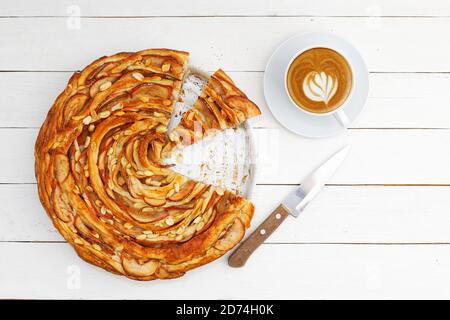 Une pâte feuilletée fraîche maison aux pommes et à la cannelle fait tourner la tarte et une tasse de café sur une table en bois blanc. Vue de dessus. Banque D'Images