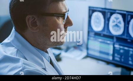 Gros plan Portrait d'un médecin professionnel regardant des images d'IRM ou d'acquisition CT sur son moniteur d'ordinateur, à la recherche de signes de tumeur au cerveau ou de cancer Banque D'Images