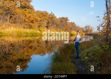 Pêche en automne sur la rivière. La jeune femme tient la canne à pêche au-dessus de la surface de l'eau. Banque D'Images