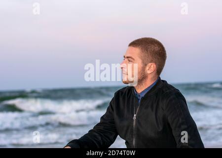 Portrait du jeune homme caucasien en profil sur fond de coucher de soleil en mer. Ambiance romantique. Banque D'Images