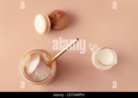 Verre de café glacé en grand verre avec paille dorée et chocolat crème et macarons, vanille sur fond pastel pour votre design. Concept alimentaire de style vintage. Style de pose à plat. Copier l'espace. Gros plan. Banque D'Images