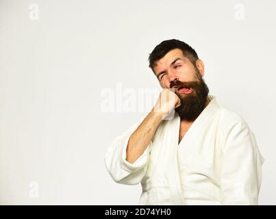 Homme de karaté avec le visage de souffrance en uniforme. Concept des arts martiaux japonais. Homme avec barbe dans un kimono blanc sur fond blanc. Le maître de Judo se frappe avec la poing Banque D'Images