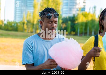 Un heureux couple noir ayant des bonbons colorés soie ensemble dans un parc d'une grande ville. Banque D'Images