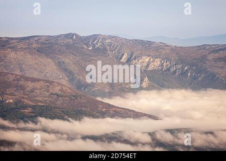 Vallée couverte par un brouillard épais allégée par la lumière dorée du matin, les collines s'élevant au-dessus du brouillard et les montagnes lointaines d'horizon Banque D'Images