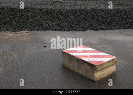 La route est fermée avec une dalle de béton armé peinte en motif d'avertissement avec des bandes diagonales rouges et blanches, derrière elles gravats empilés pour la surface de la route Banque D'Images