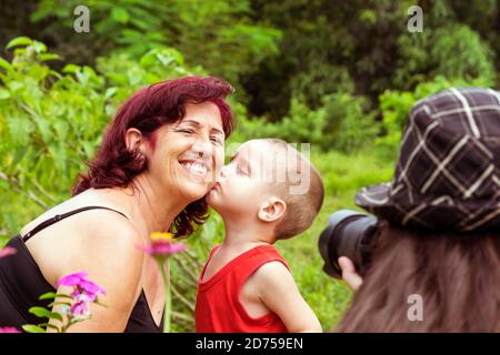 Un petit enfant de trois ans embrasse sa grand-mère dans la joue pendant elle est photographiée par une photographe féminine dans un Jardin cubain Banque D'Images