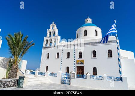 Eglise orthodoxe à Oia, Santorin, Grèce, un jour d'été avec drapeau grec. Beau ciel bleu clair. Banque D'Images