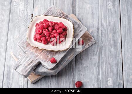 Fruits à la framboise dans une assiette sur de vieilles planches à découper, pile saine de baies d'été sur fond de bois gris, vue en angle Banque D'Images