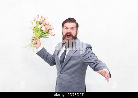 Des vacances de haine. Journée pour femme. 8 Mars. Homme barbu en colère avec des fleurs. Fêtez le printemps. Échec de la date. Irritée, l'homme barbu agacé avec bouquet de tulipes. Concept déçu. Date d'échec. Banque D'Images