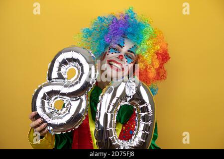 Clown se tenant sur fond jaune insolé jaune et portant un numéro 80. Concept de célébration. Banque D'Images