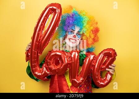 Clown se tenant sur fond jaune insolé jaune tenant le mot amour. Banque D'Images