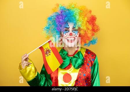 Clown se tenant sur fond jaune insolé jaune tenant le drapeau espagnol. Banque D'Images