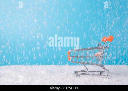 Concept météo joyeux shopping. Vue rapprochée du profil de côté photo de petit chariot miniature en argent et chute de neige Banque D'Images