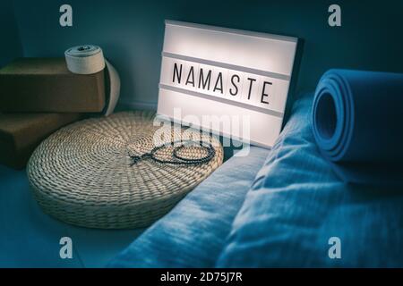 Visionneuse de panneau de classe de studio de yoga avec lettres écrivant NAMASTE luminescent dans la nuit avec des accessoires naturels, tapis en caoutchouc, blocs de liège, organique Banque D'Images