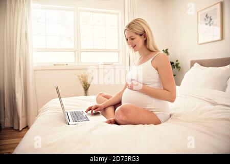 Belle jeune femme enceinte avec un ordinateur portable sur le lit Banque D'Images