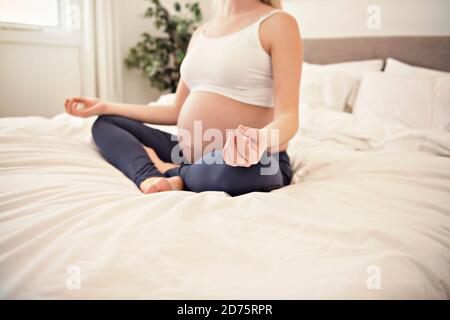 Femme enceinte faisant de l'exercice de yoga sur le lit Banque D'Images