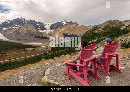 Homme et femme assis sur des chaises rouges et prenant la vue du sentier Wilcox dans le parc national Jasper, Alberta, Canada. Banque D'Images