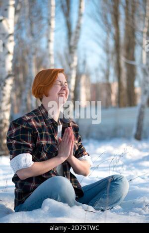 Belle jeune femme assis dans la forêt gelée et sourires. Jour d'hiver en vacances, en plein air. Banque D'Images