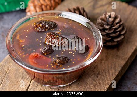 Les jeunes cônes de pin se coince dans un bol en verre sur une planche en bois. Confiture délicieuse avec les petits cônes de pin. Banque D'Images